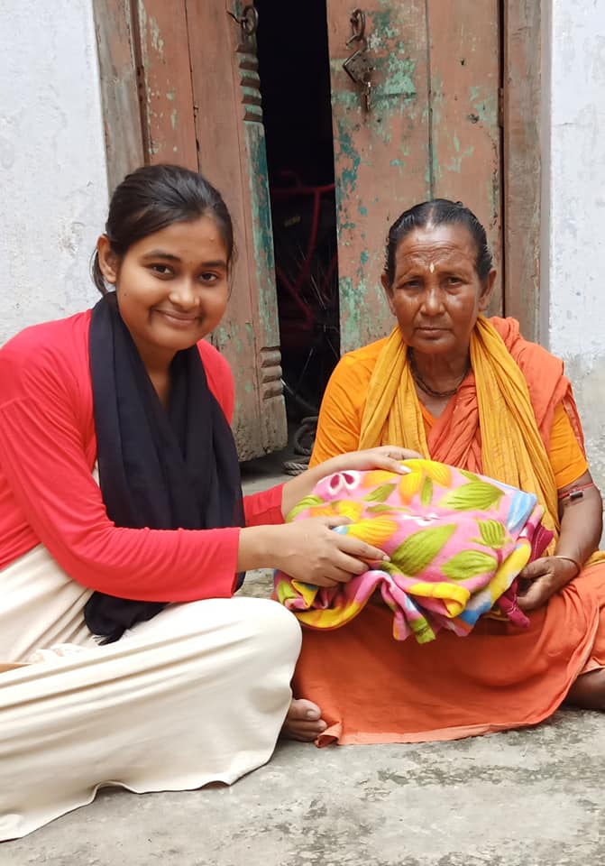 Shreyasi handing a blanket to a woman in Domar, Nilphamari.