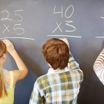 Rear view of children solving math equation on chalkboard