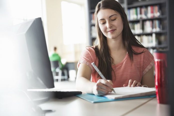 female-student-writing-notes-in-binder-in-college-library